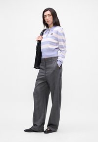 Polo cu dungi violet deschis și alb, cu guler, asortat cu pantaloni gri cu dungi subțiri și pantofi negri fără toc. Modelul ține o jachetă neagră.