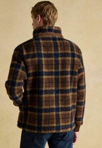 Brown and navy plaid fleece jacket with high collar. Textured surface and elastic cuffs. Retains warmth, designed for casual wear.