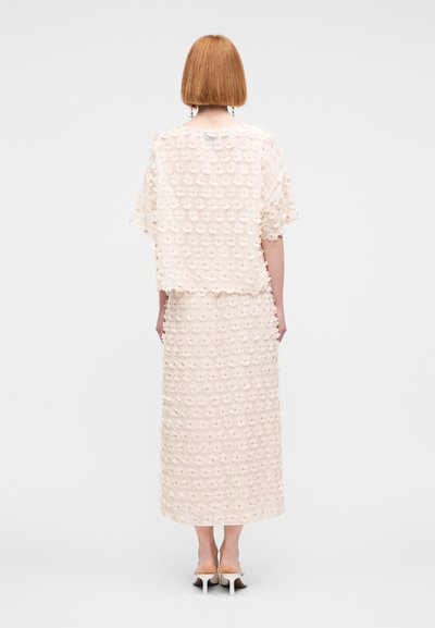 Σετ ανοιχτό ροζ φόρεμα και τοπ με υφή λουλουδένιου μοτίβου, με χαλαρή εφαρμογή και φούστα μέχρι τον αστράγαλο. Το σύνολο ολοκληρώνουν λεπτά παπούτσια με τακούνι.