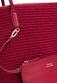 Borsa a rete rossa con un esterno testurizzato, dotata di accenti in pelle e una tasca con zip dorata con dettagli in rilievo del logo.