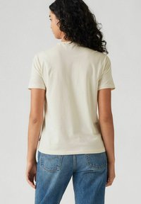 Lichtbeige katoenen T-shirt met korte mouwen, een ronde halslijn en een relaxte pasvorm. Gecombineerd met blauwe denim jeans. Soepele textuur, minimale details.