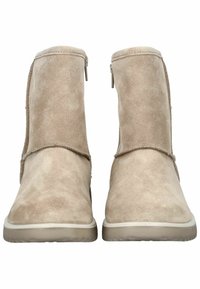 Botines de ante beige con una textura suave, que cuentan con una cremallera lateral para el cierre y un diseño sencillo con suelas de goma blanca.