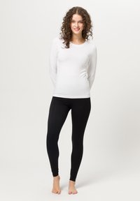 Top bianco a maniche lunghe abbinato a leggings neri. Il top è in tessuto morbido, con scollatura rotonda; i leggings sono aderenti e di texture morbida.
