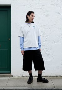 Valge T-särk, millel on värvikas graafika, kantud helesinise pika varrukaga särgi peal. Komplekti kuuluvad mustad laiad lühikesed püksid ja mustad kingad.