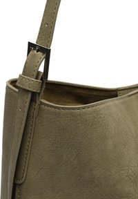 Primer plano de un bolso de cuero verde oliva texturizado con una correa ajustable asegurada por una hebilla cuadrada plateada.