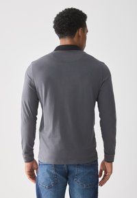 Long-sleeve polo shirt in dark gray with a black collar. Made from smooth fabric, featuring a straight hem and fitted sleeves.