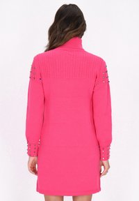 Fuchsia sweaterjurk met een col, geribbelde textuur op de schouders en versierde mouwen met kleine gekleurde studs.
