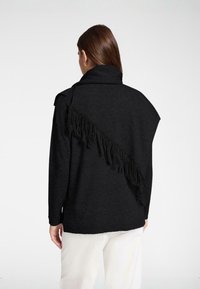 Schwarzer Strickpullover mit einem drapierten Schalkragen und diagonalen Fransen auf der Rückseite. Verfügt über lange Ärmel und eine lockere Passform.