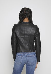 Czarna skórzana kurtka o dopasowanym kroju, z przeszyciami i wysokim kołnierzem. Połączona z jasnoniebieskimi dżinsami.