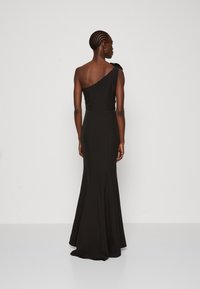 Rochie neagră, cu un umăr, cu un bust ajustat și o fustă evazată. Prezintă o țesătură texturată și un accent sub formă de fundiță pe umăr.