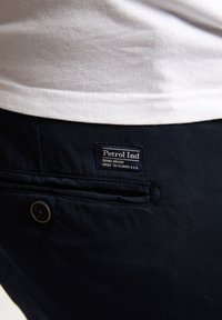 Marineblauwe broek van geweven stof met een voorzak en knoopdetail. Voorzien van een label met de tekst "Petrol Ind" op de achterkant.