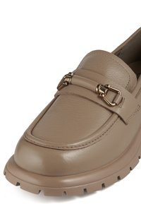 Beige leren instapper met een ronde neus, brede band en metallic hardware accent. Voorzien van een dikke, gewatteerde rubberen zool voor grip.