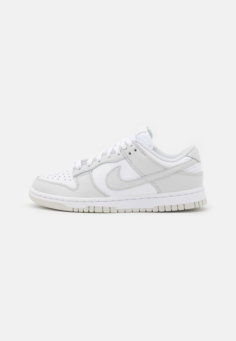 White Nike sneakers featuring leather and textile materials, a low-top design, perforated toe box, and a gray accent on the side.