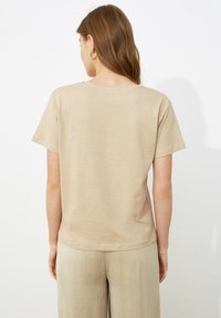Camiseta beige de manga corta con un corte relajado, hecha de una tela suave. Presenta un escote redondo y una textura lisa, combinada con pantalones a juego.