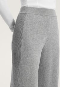 Svetlo sivi pleteni hlače z gladko teksturo, ki imajo rebraste detajle ob straneh in elastičen pas.