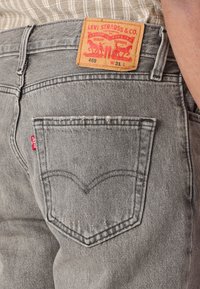 Sivi traperice klasičnog kroja, s kožnom etiketom s natpisom "Levi Strauss & Co." i prepoznatljivim dizajnom stražnjeg dzepa.
