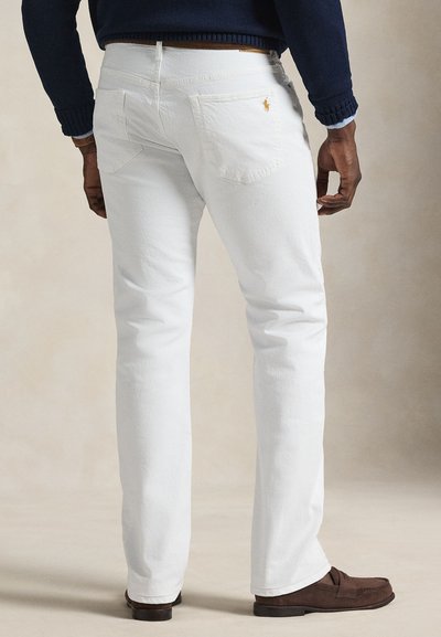 Λευκά βαμβακερά τζιν με ευθεία γραμμή, που διαθέτουν δύο πίσω τσέπες και ένα μικρό λογότυπο στην δεξιά τσέπη. Φορεμένα με καφέ παπούτσια.