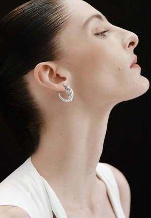 Pendientes en forma de media luna de plata con un diseño texturizado, que presentan pequeños acentos claros, llevados por una persona con un peinado elegante.