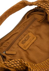 Tan leren handtas met een gestructureerde buitenkant, een ritscompartiment en een binnenlabel. Heeft een zachte, gemusterde voering.