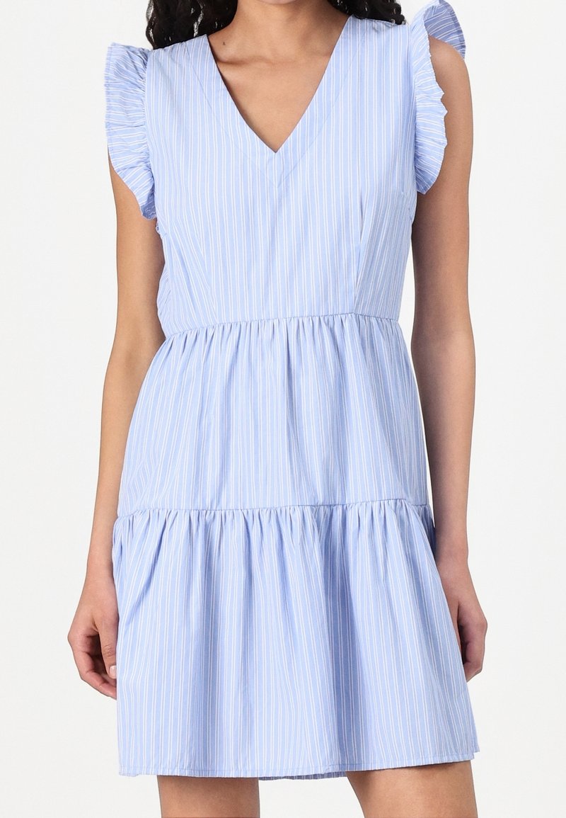 Femme portant une robe bleu clair sans manches avec des rayures verticales blanches, des détails froncés aux épaules et une taille et une jupe froncées.