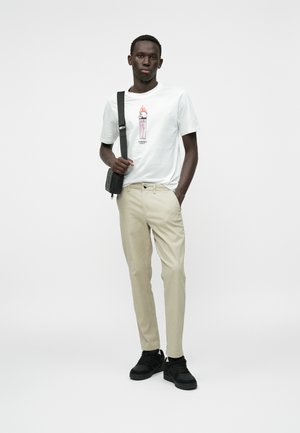 Hvit t-skjorte med grafisk trykk, beige bukser og svarte joggesko. Hvordan den tilbehøret inkluderer en svart crossover-veske. Enkel design og uformell passform.