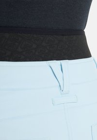 Jasnoniebieskie spodnie o gładkiej fakturze, z wysokim czarnym pasem w subtelny wzór serc oraz kontrastowym przeszyciem u góry.