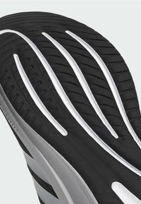 Black shoe sole with white accent grooves, featuring textured rubber for grip and stability. Side displays grey and black striped design.