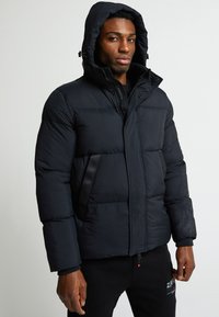 Pūšļa jaka tumši zili, ar kapuci, ar rāvējslēdzēju priekšā un ar pogām aizveramā. Tekstūrēta auduma un divām sānu kabatām ar kontrastējošu detaļu.