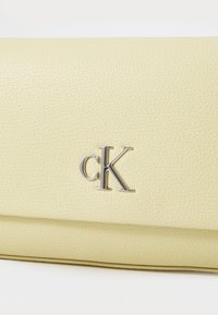 Portefeuille en cuir texturé jaune avec un logo "cK" argenté à l'avant et un design épuré et minimaliste. Fini lisse et forme compacte.