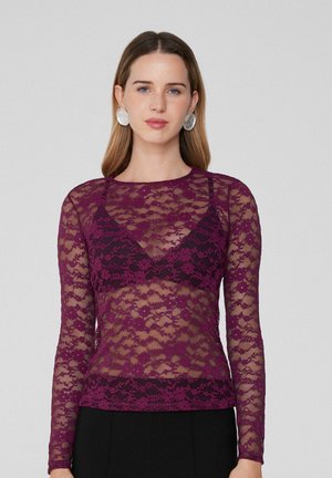 Purple lace long-sleeve top with a floral pattern and sheer quality, layered over a black undergarment, paired with large silver earrings.