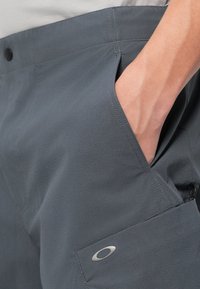 Γκρι υφασμάτινα παντελόνια με υφή, που διαθέτουν πλαϊνή τσέπη και διακριτή λεπτομέρεια λογότυπου. Η μέση περιλαμβάνει κλείσιμο με κουμπί.