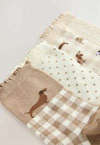 Three pairs of socks featuring light brown, white, and cream colors. Textures include ribbed and patterned designs with dachshund motifs.