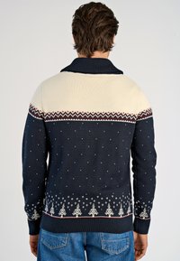 Granatowy sweter dzianinowy z kością słoniową w górnej części, ozdobiony wzorami w zygzak oraz płatkami śniegu, z małymi białymi kropkami i motywami drzew na dole.