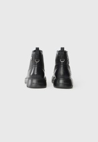 Boots negre din piele până la gleznă, cu o textură netedă, având bucle pentru tragere, accente cu hardware argintiu și o talpă cushioned. Logo-ul brandului pe spate.