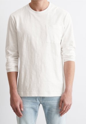 Langärmeliges T-Shirt mit Rundhalsausschnitt aus hellcremefarbenem Baumwollstoff, mit einer linken Brusttasche vorne und einer lockeren Passform mit umgeschlagenen Ärmeln.