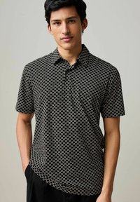 Camicia a maniche corte, con colletto, di colore nero con motivi geometrici bianchi. Realizzata in materiale leggero, presenta una tasca sul petto.