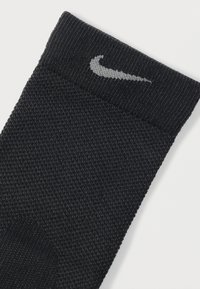 Μαύρη αθλητική κάλτσα με υφασμάτινη υφή, που διαθέτει πλεκτό πάνω μέρος και γκρι λογότυπο Nike στον περιλαίμιο.