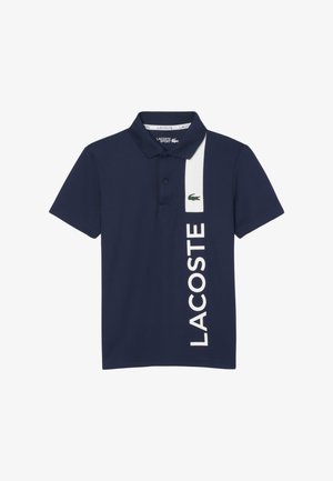 Marineblauwe polo van katoen, voorzien van een witte verticale streep met de tekst "LACOSTE" en een groene krokodil op de linkerzijde.