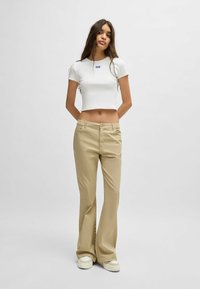 White cropped t-shirt with a small blue logo. Light beige flared trousers with a smooth texture, featuring front pockets and button closure.