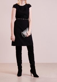 Czarna sukienka bez rękawów z dopasowanym wcięciem w talii i srebrnym paskiem z ćwiekami, w zestawieniu z wysokimi na kolana czarnymi zamszowymi botkami oraz metaliczną kopertówką.