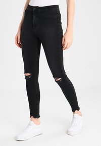 Svarta högmidjade skinny jeans med slitna knäskärningar, rå nederkant och fem fickor. Tillsammans med vita sneakers för kontrast.