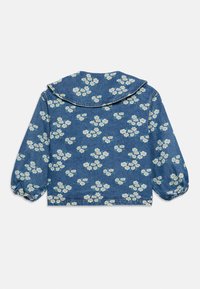 Veste en denim avec imprimé floral de marguerites blanches et jaunes, grand col arrondi et poignets élastiques sur les manches longues, vue de dos.