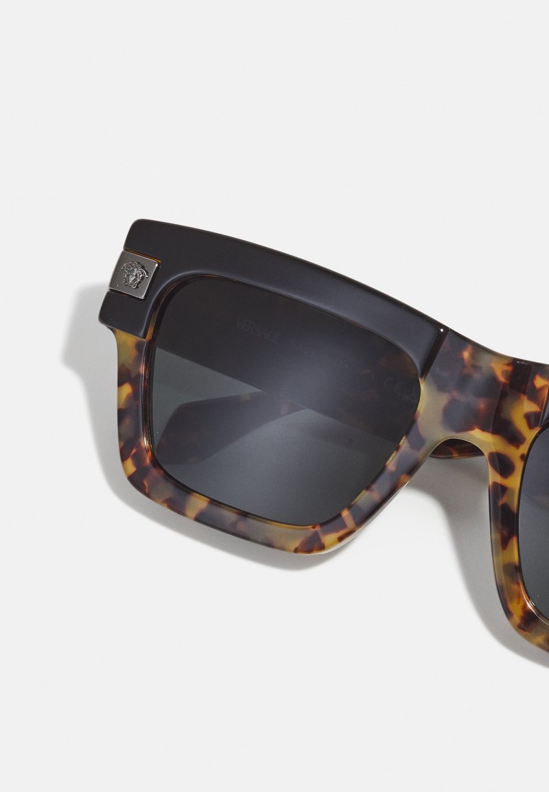 Fyrkantiga solglasögon med sköldpaddsmönstrade bågar och mörka linser. Har guldutrustning med en logodetalj på sidan. Tillverkade av plast.