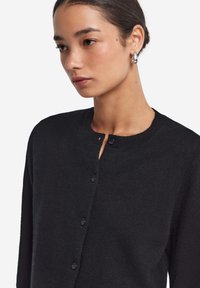 Czarny dziany kardigan z okrągłym dekoltem, z przodu na guziki i długimi rękawami. Miękka faktura i minimalistyczne detale.