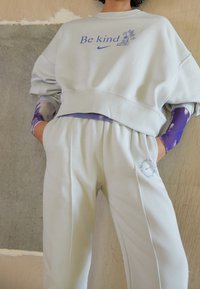 Ljusgrå bomullströja och matchande joggers med texten "Var snäll" och blommig grafik. Har en avslappnad passform och subtila lila accenter.