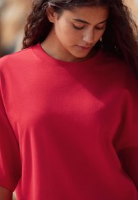 Rød oversized t-shirt med korte ærmer og ribbet nakkekrave, lavet af blødt bomuldsstof, der har en glat tekstur og en afslappet pasform.