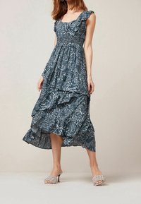 Robe maxi florale bleue avec des bretelles à volants, un design à étages et un corsage froncé. Portée avec des sandales à glissière tissées beiges.