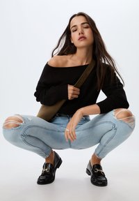 Črna off-shoulder sv sweater, svetlo modri raztrgani skinny jeans z raztrganimi koleni in črne loafers s podrobnostjo z zlatim verigo.