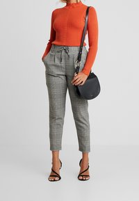 Orange randig tröja med hög hals, kombinerad med grå rutiga byxor med dragsko i midjan och sidofickor. Svart crossbody-väska och remsandaler.