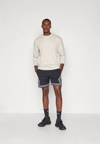 Felpa grigia con un piccolo logo, abbinata a pantaloncini neri in rete con bordi bianchi, calze nere e sneakers nere.